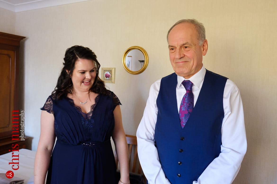 bridesmaid and father of bride look on as bride gets ready