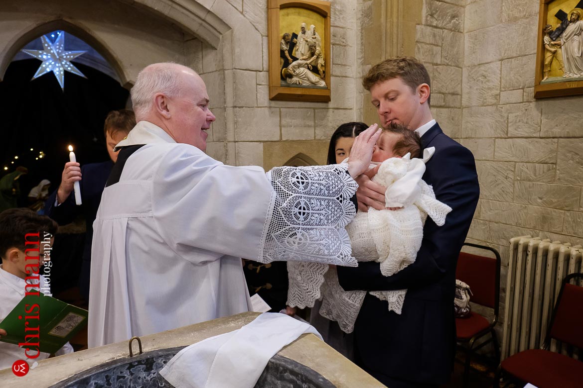 Father Sean Finnegan blesses child at baptism ceremony Sacred Heart Church Caterham