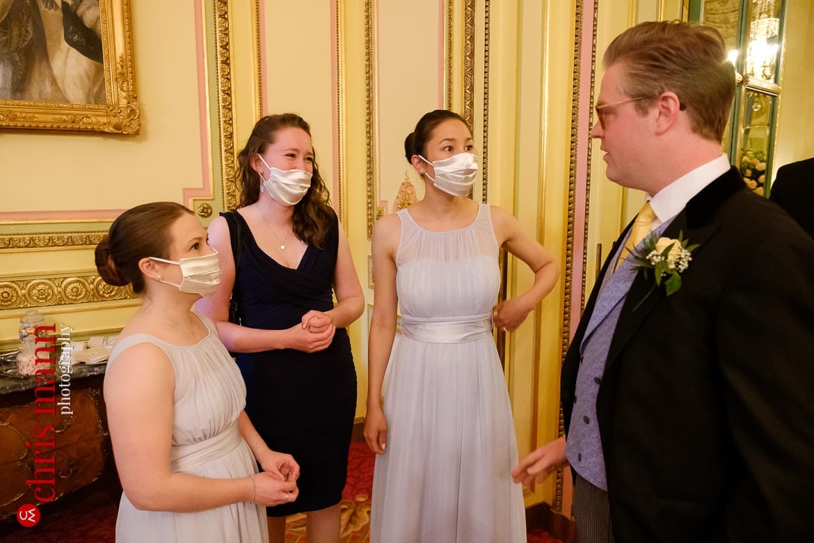 Groom chatting to mask-wearing bridesmaids - Ritz London wedding photography - Covid restrictions